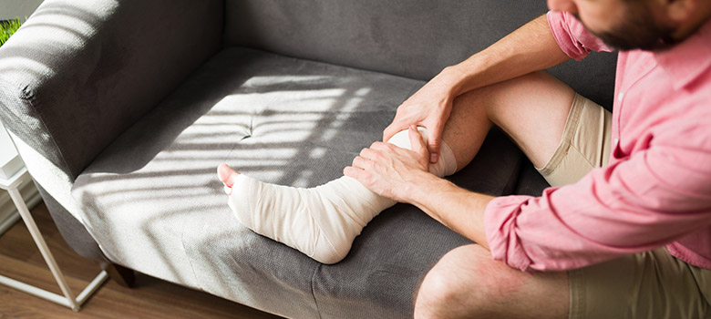 Homme à la cheville bandée assis sur son canapé - La Prévention Médicale