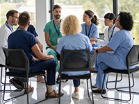 Un groupe de soignants discutent. Ils sont assis en cercle dans une salle lumineuse de l'hôpital - La Prévention Médicale